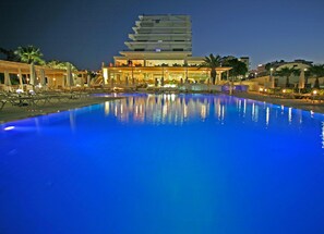 A modern hotel with a large swimming pool, outdoor seating, and a multi-story building. - Vrissiana Boutique Beach Hotel (Paralimni)