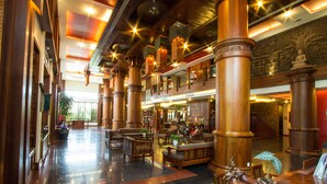 A spacious lobby with high wooden columns, seating areas, and a staircase leading to an upper level.