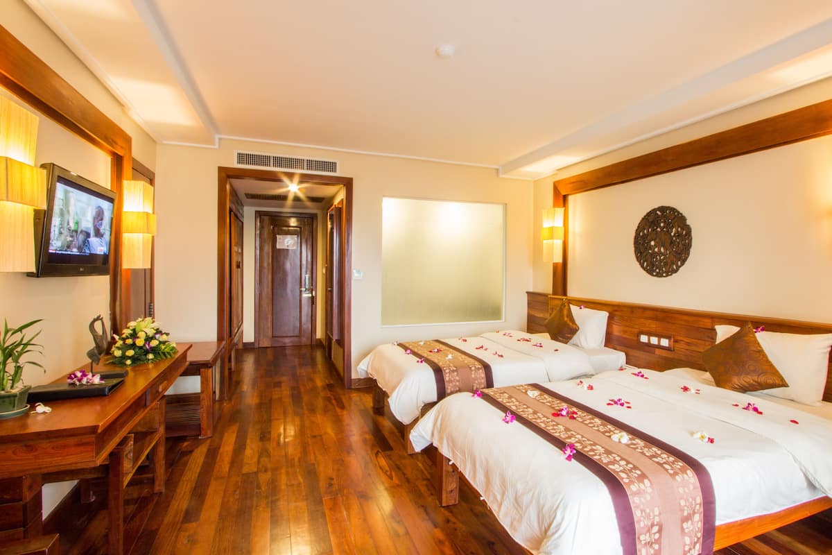 Habitación de hotel con dos camas, suelo de madera, televisión y un escritorio con una planta.