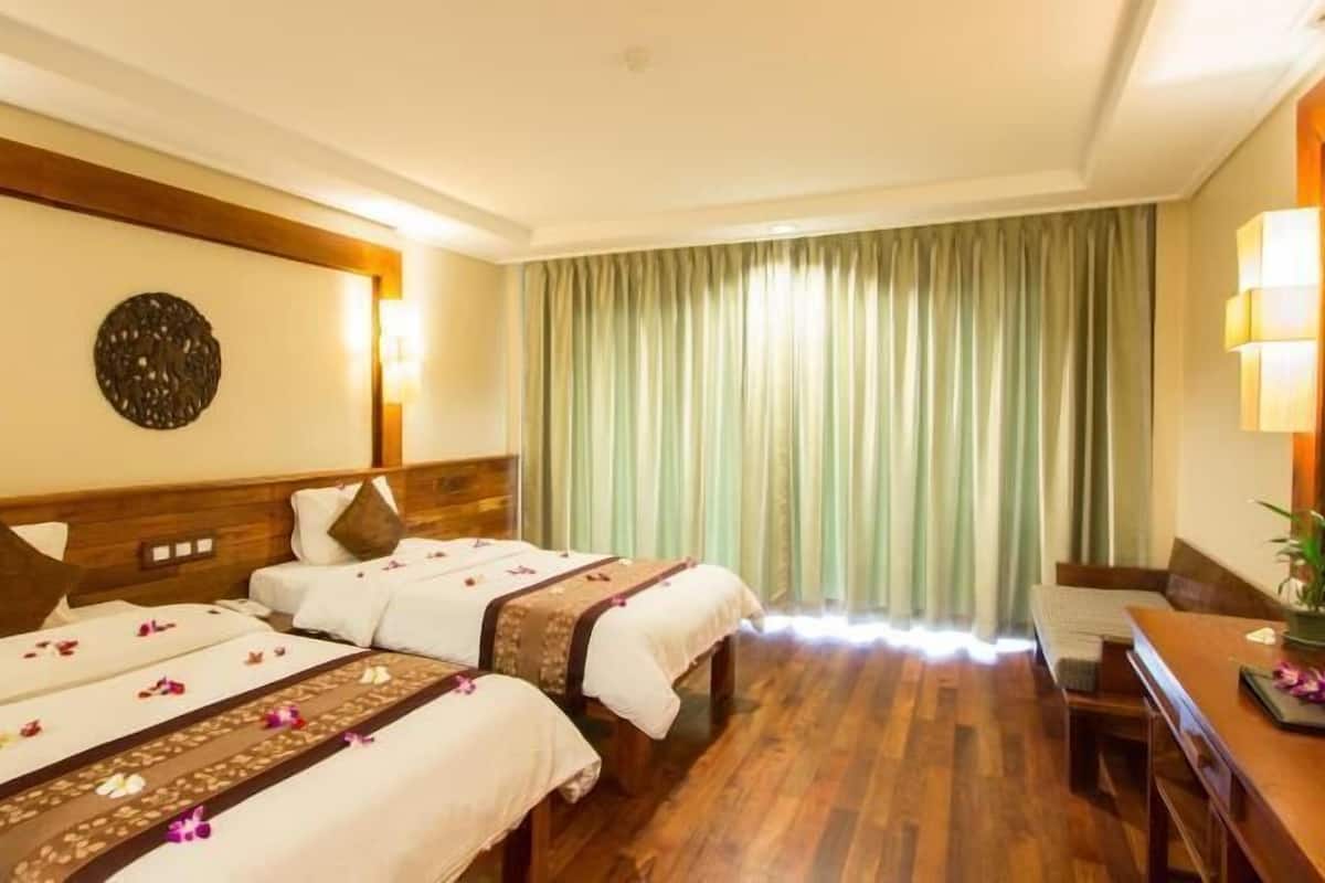 Habitación de hotel con dos camas, cabecero de madera, un espejo grande, un escritorio con una silla y vistas al exterior a través de cortinas traslúcidas.