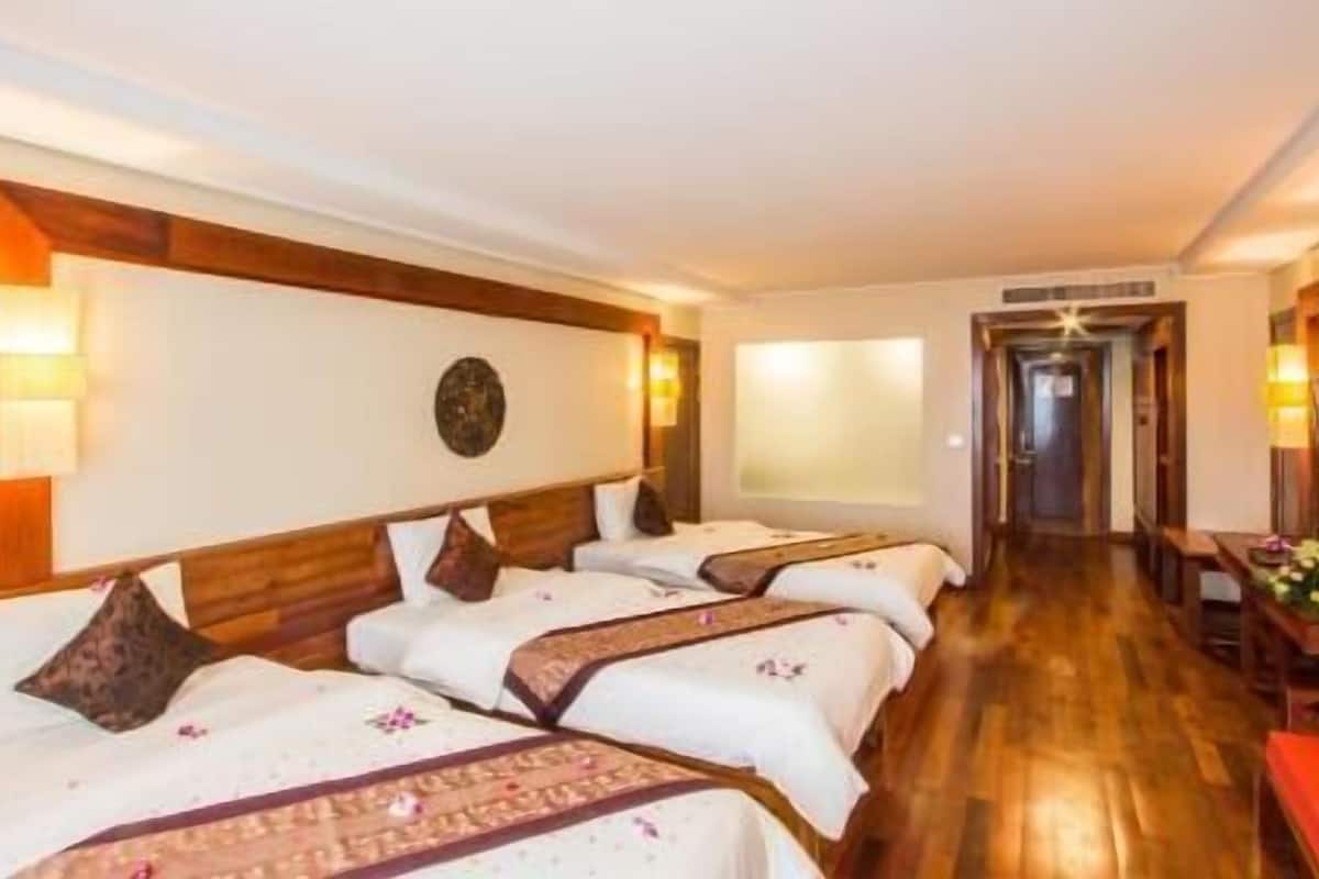Habitación de hotel con cuatro camas, un cabecero de madera, un reloj de pared y un pasillo que conduce a otra habitación.