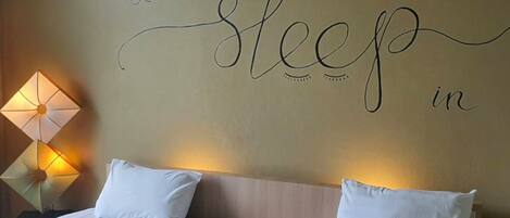 A hotel room with two beds, a wall with the phrase "Let's sleep in" and a decorative lamp.