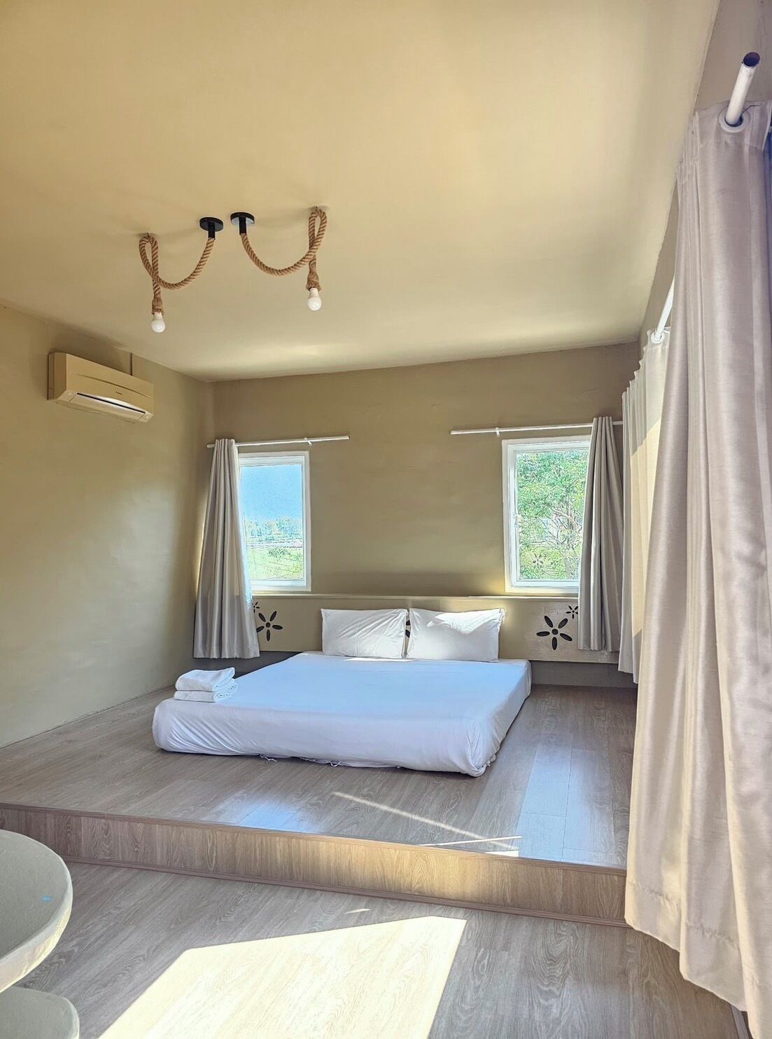 Un dormitorio con una cama, dos ventanas con cortinas, un equipo de aire acondicionado y un candelabro.