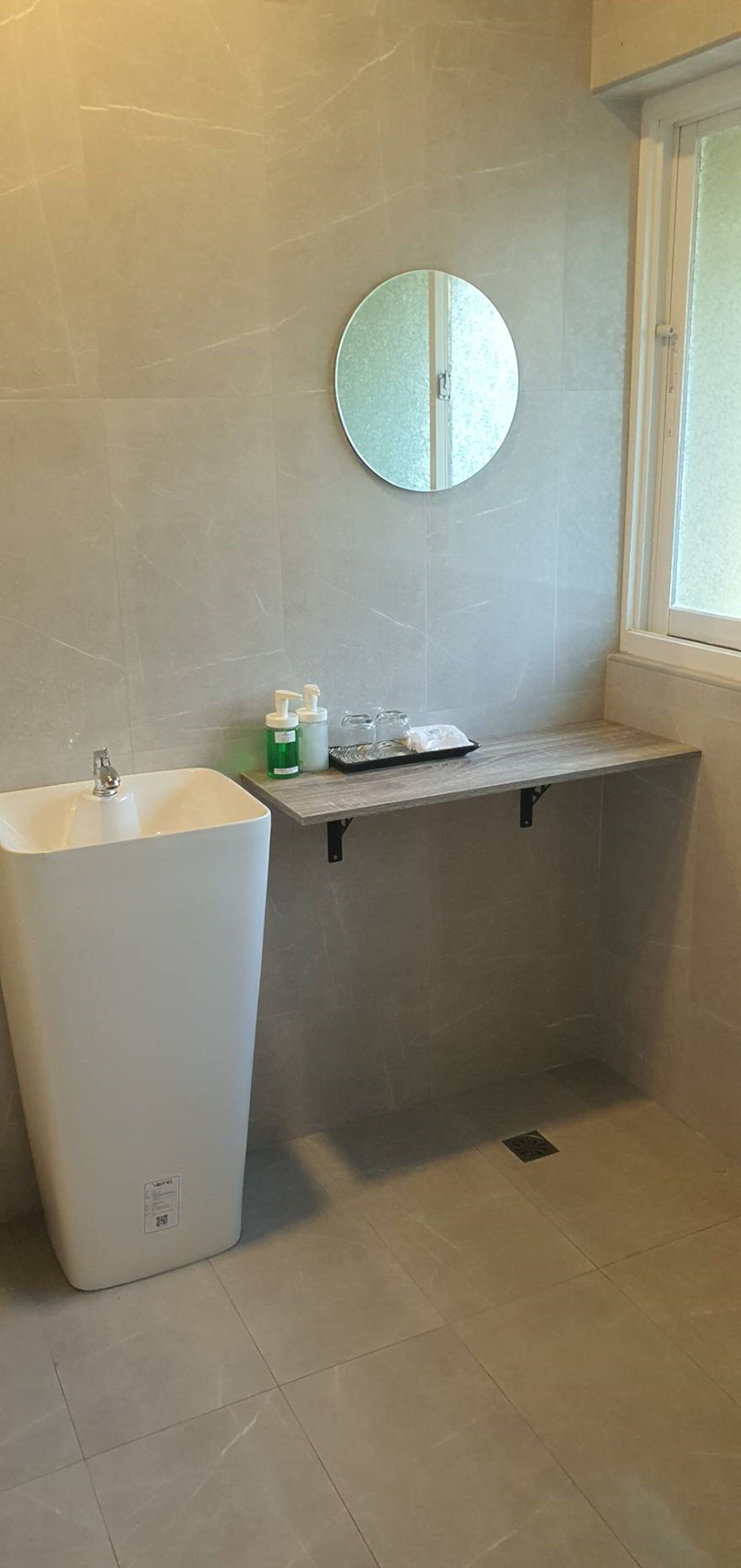 Une salle de bain avec un lavabo sur colonne, un miroir et une étagère contenant des articles de toilette.