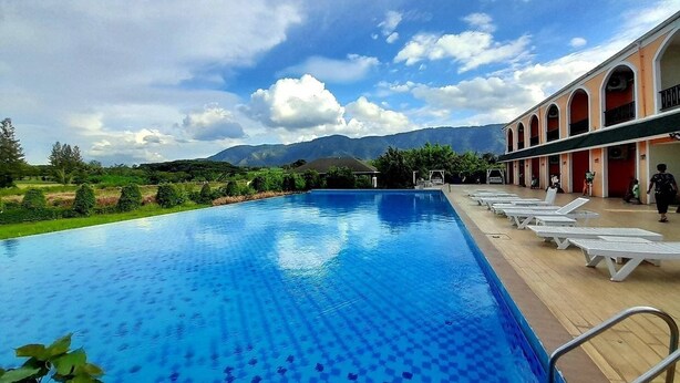 A swimming pool with a tiled deck, surrounded by a building with arched windows and a view of mountains.