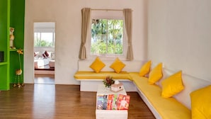 A bright living room with a yellow sofa, a coffee table with books, and a window with curtains.