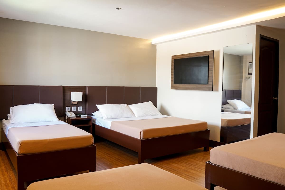 Habitación de hotel con dos camas individuales, una mesita de noche con teléfono, un televisor montado en la pared y un espejo.