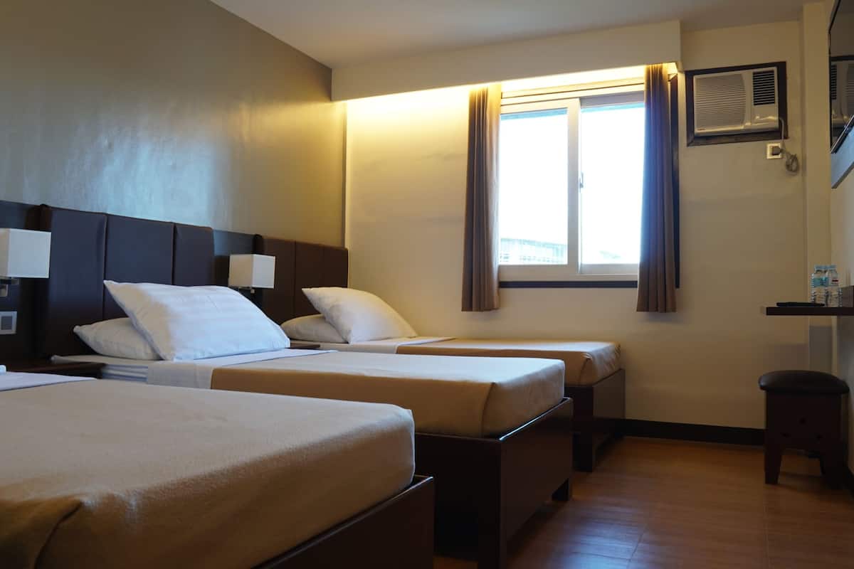 Habitación de hotel con dos camas, una ventana con cortinas, un taburete pequeño y un estante con botellas de agua.