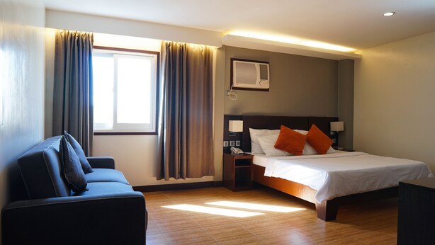 Habitación de hotel con cama, escritorio, silla, ventana con cortinas y aire acondicionado de pared.