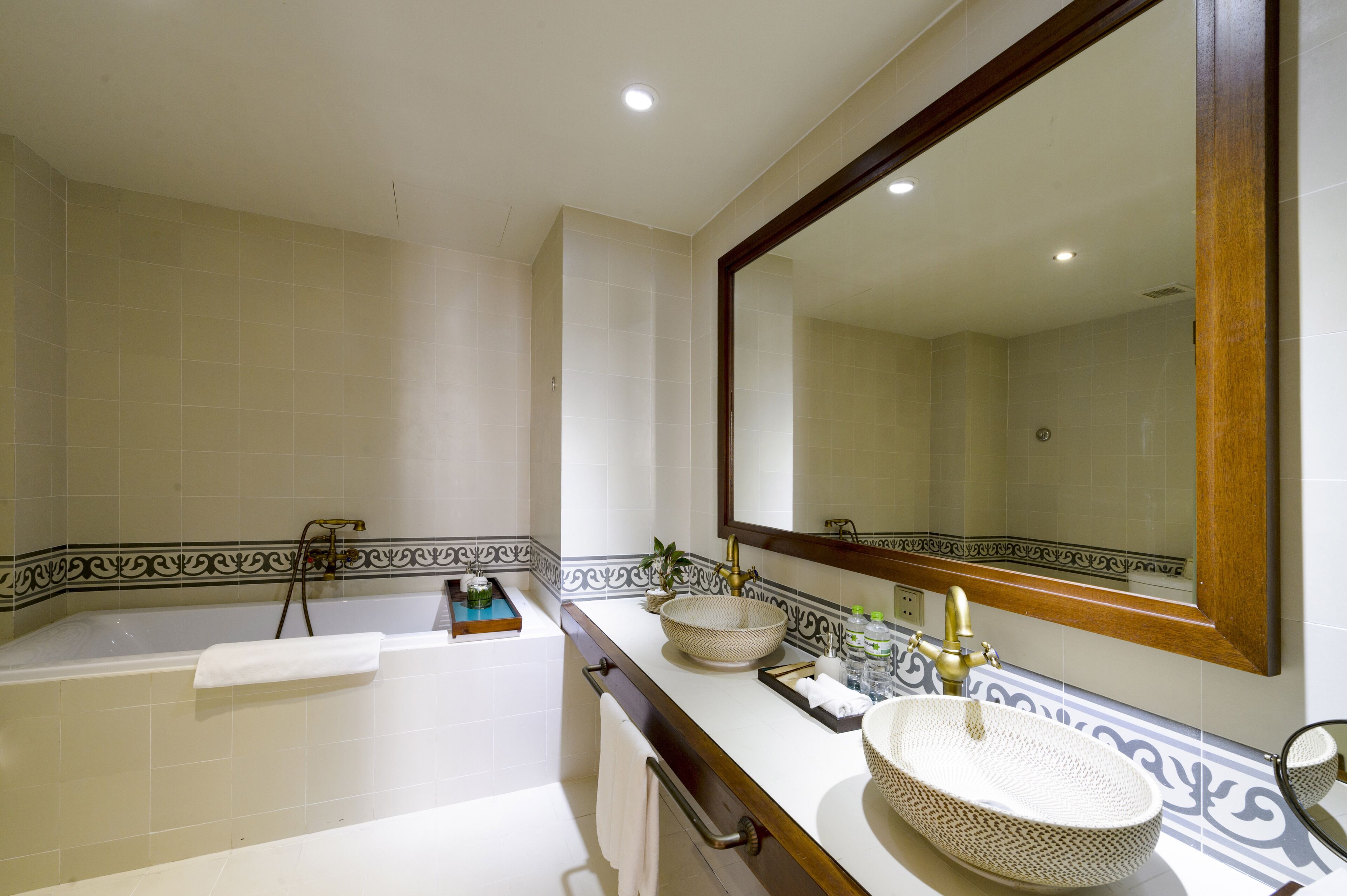 Un baño con bañera, un espejo grande y un tocador con lavamanos y adornos.