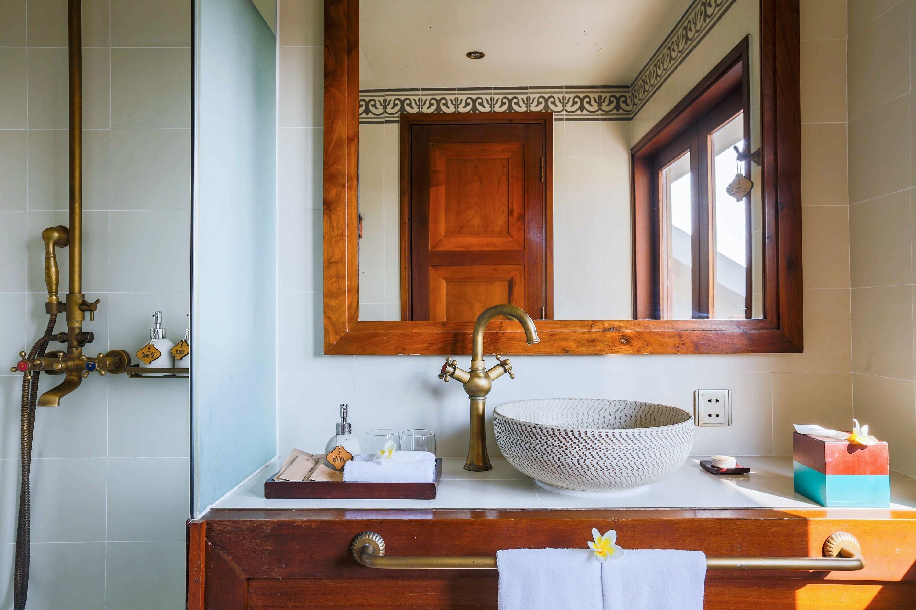 Un baño con tocador de madera, un espejo grande, un grifo de latón, un lavabo sobre encimera y un perchero para toallas.