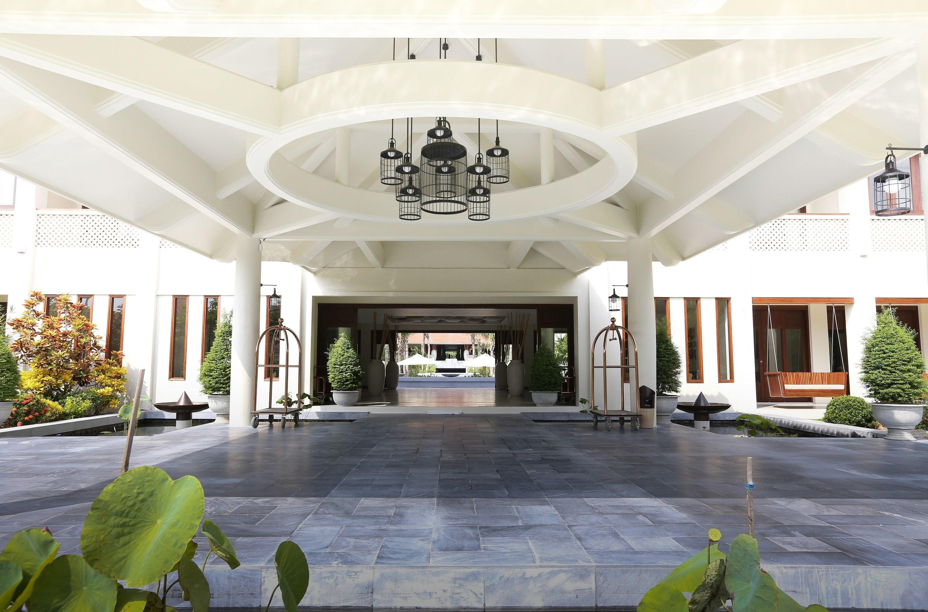 A spacious lobby with a high ceiling and a central chandelier, leading to a building entrance.