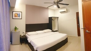 Quarto com cama, mesa de cabeceira, pequena geladeira, ventilador de teto, aparelho de ar condicionado e porta.
