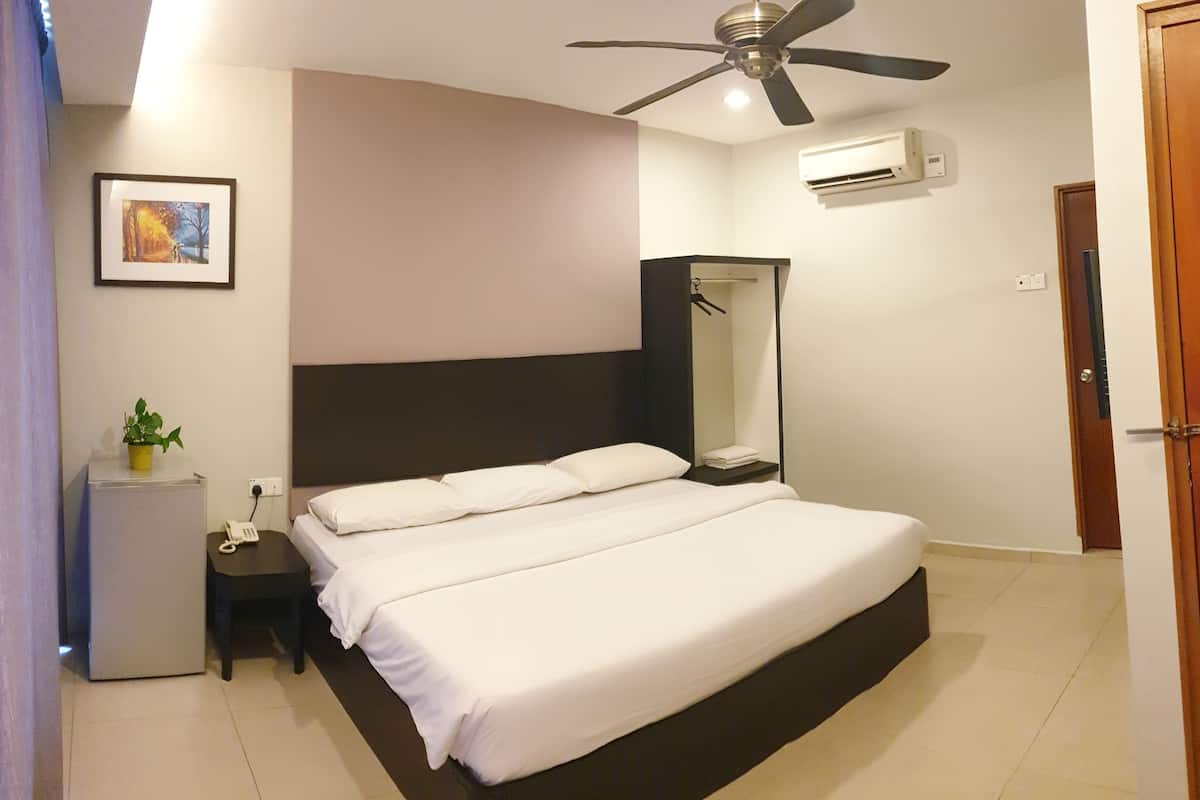 A bedroom with a bed, bedside table, a small fridge, a ceiling fan, an air conditioning unit, and a door.