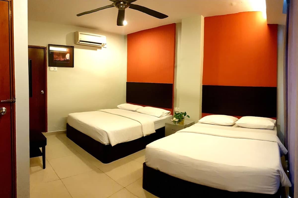 A hotel room with two single beds, a ceiling fan, an air conditioning unit, and a small table with a vase of flowers.