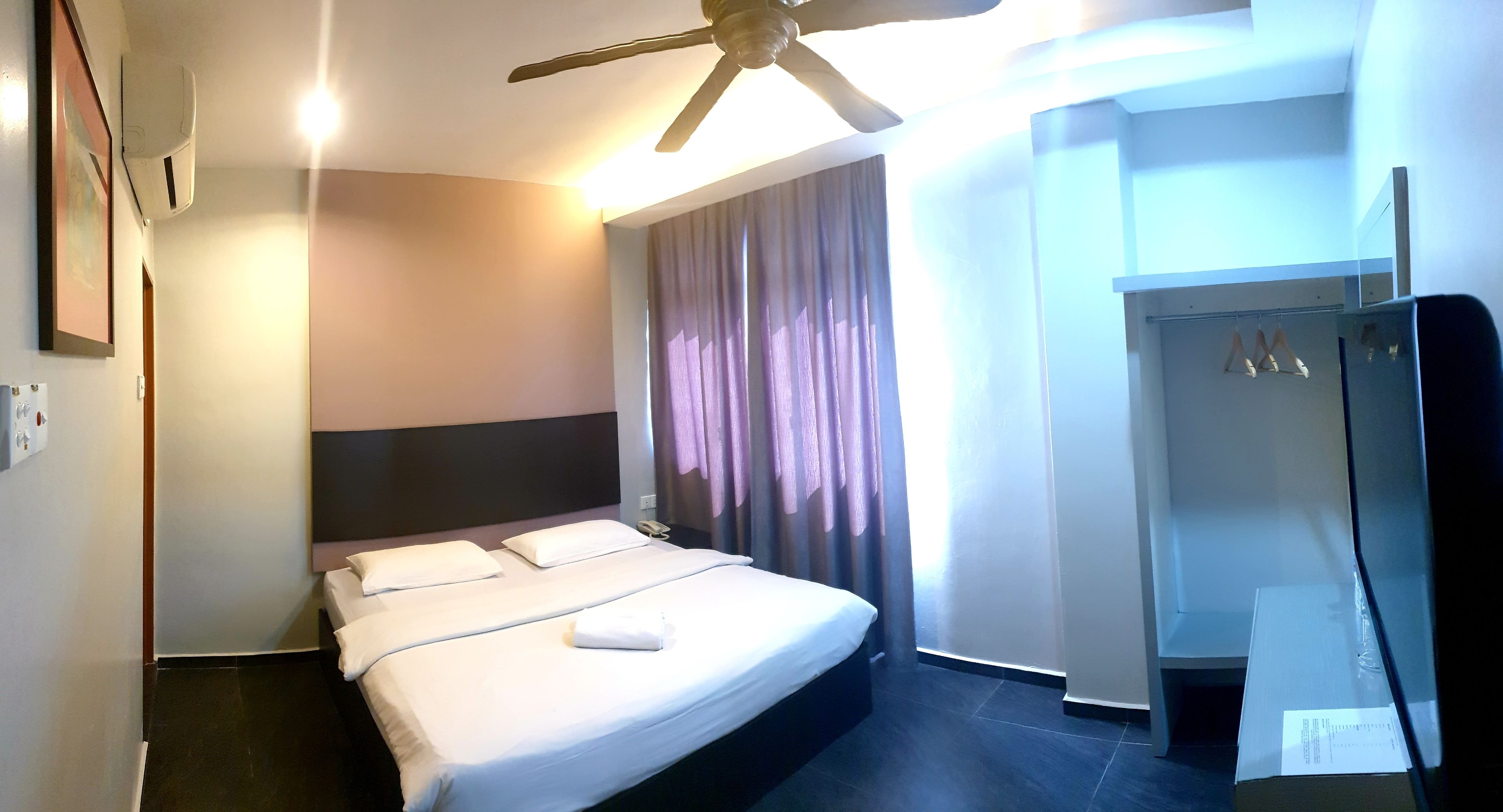 Ein Hotelzimmer mit Bett, Deckenventilator, Duschbereich und einem fenster mit Vorhängen.