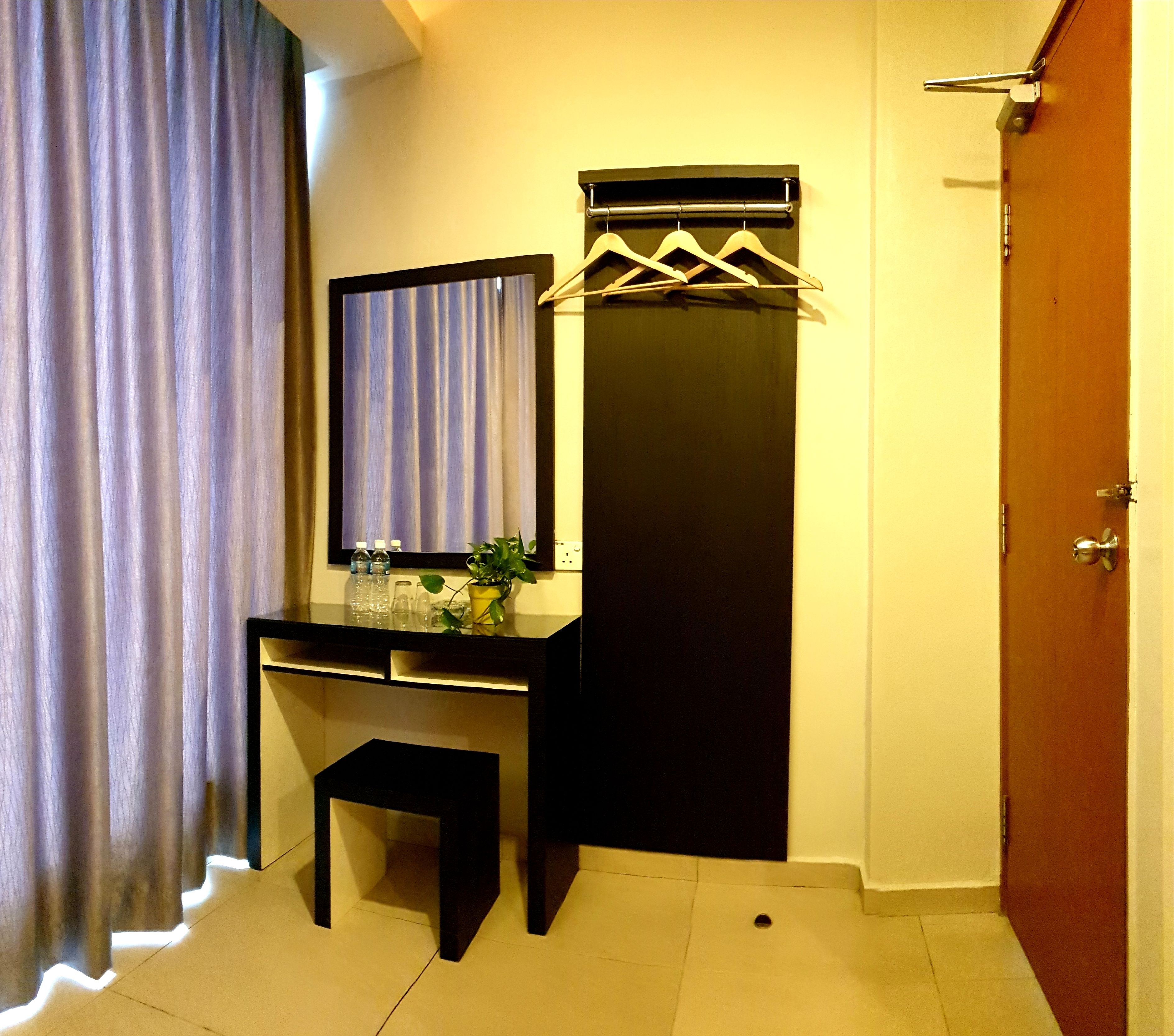 Quarto compacto com escrivaninha escura, espelho e um cabideiro.