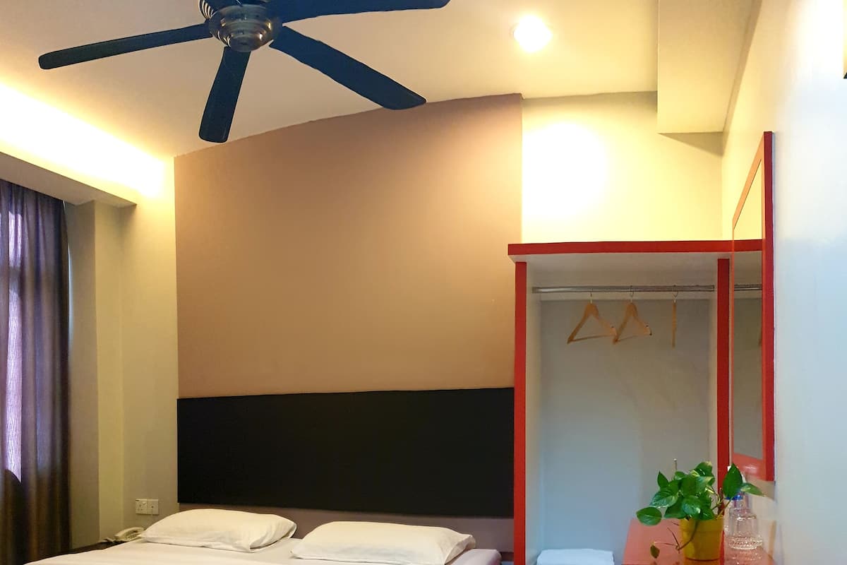 A hotel room with a bed, a ceiling fan, a bedside table with a mirror, and a small plant.
