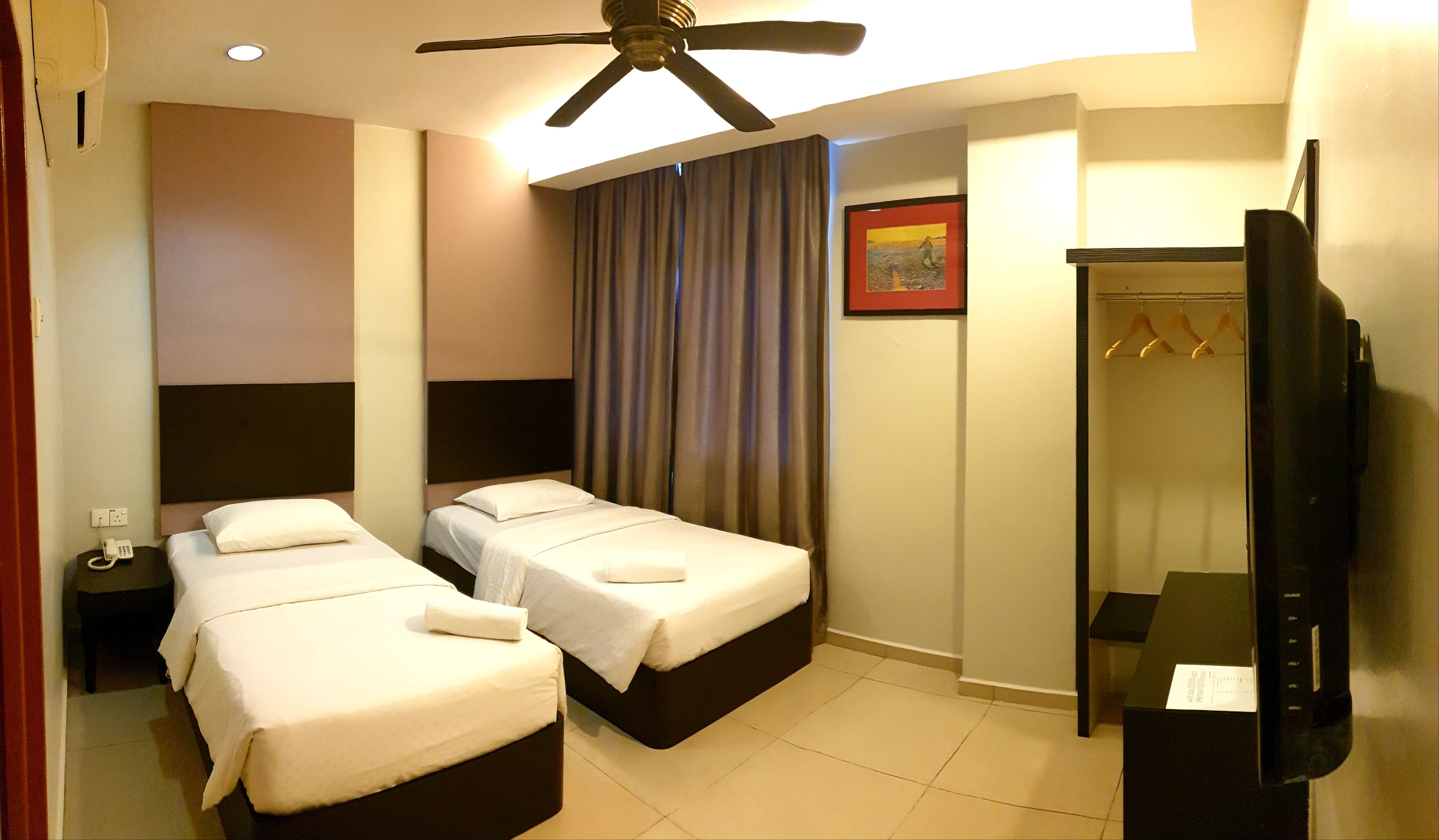 A hotel room with two beds, a ceiling fan, a TV, a coat rack, and a painting on the wall.