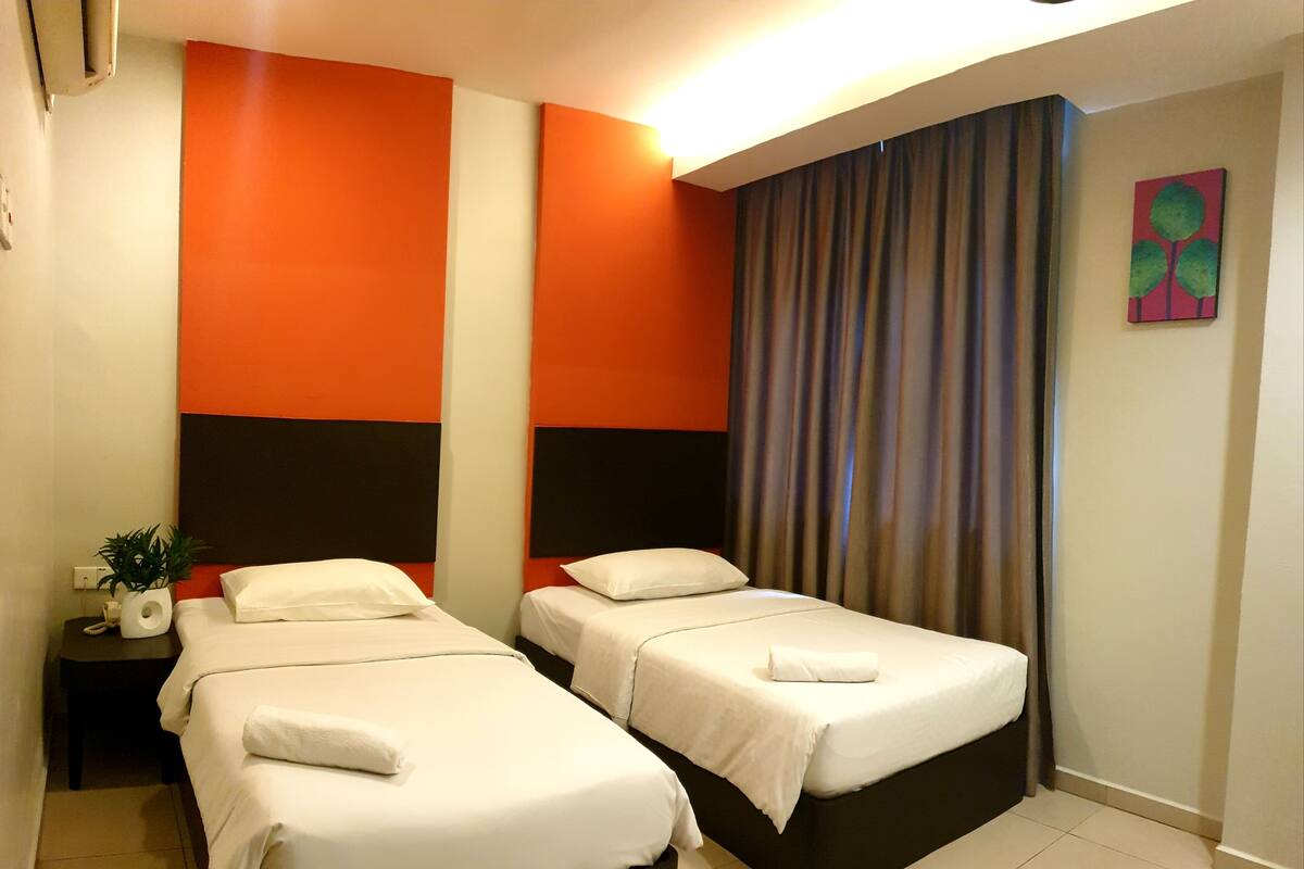 A hotel room with two beds, a nightstand with a plant, and a painting on the wall.