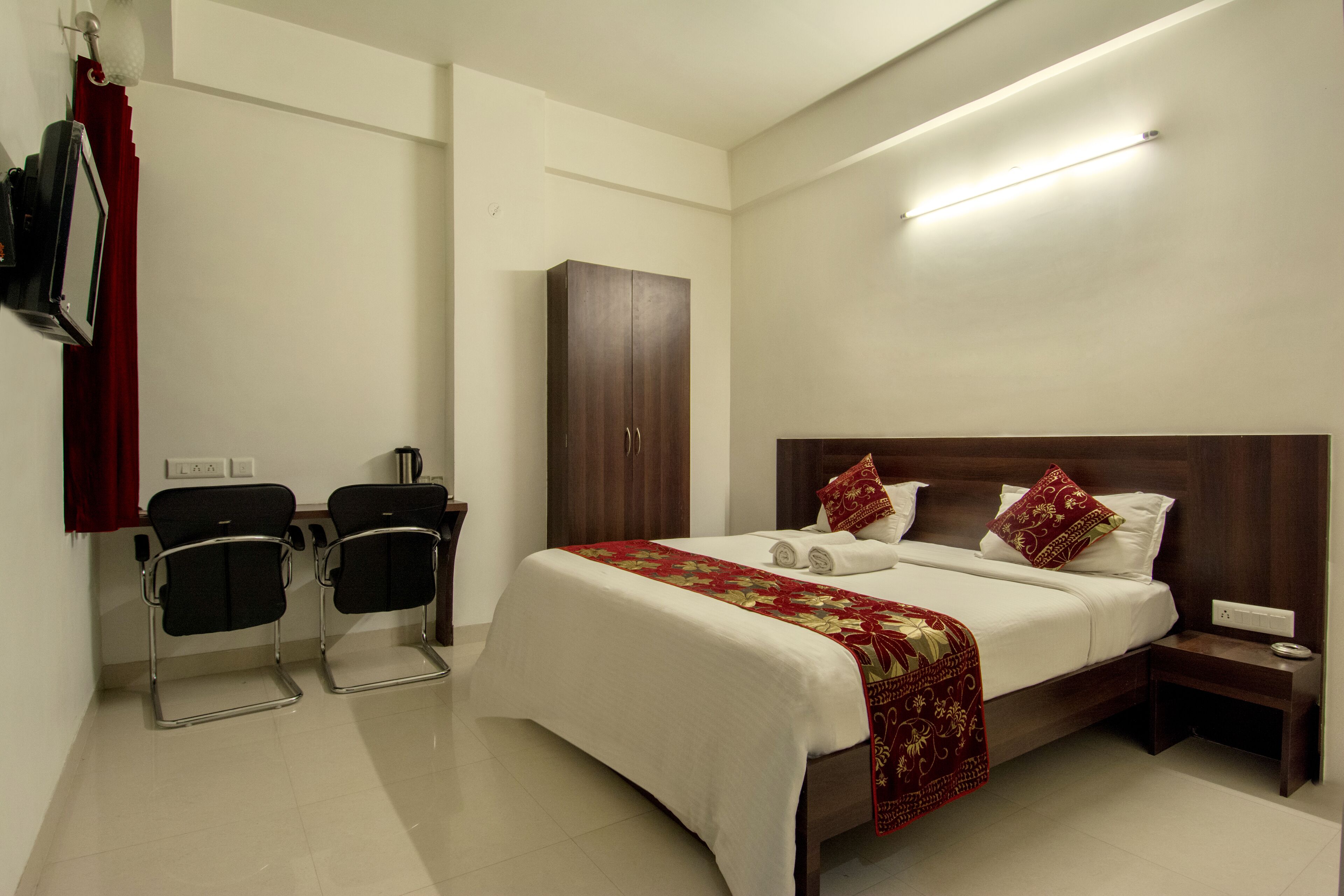 A hotel room with a bed, a nightstand, a wardrobe, two chairs, and a desk with a chair.