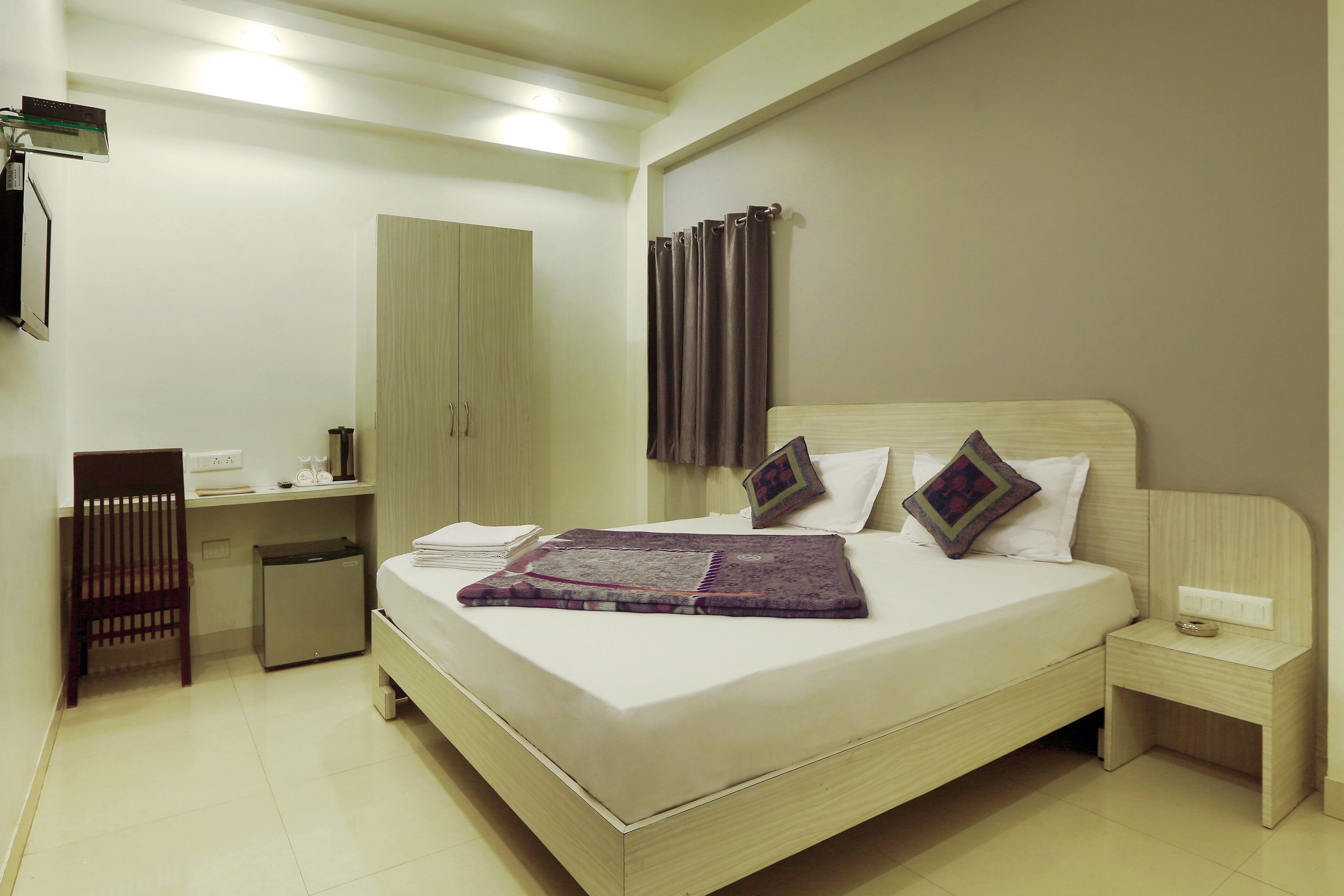 Une chambre d’hôtel bien rangée, avec un lit, une table de chevet, une commode, un bureau, une chaise et un petit placard.