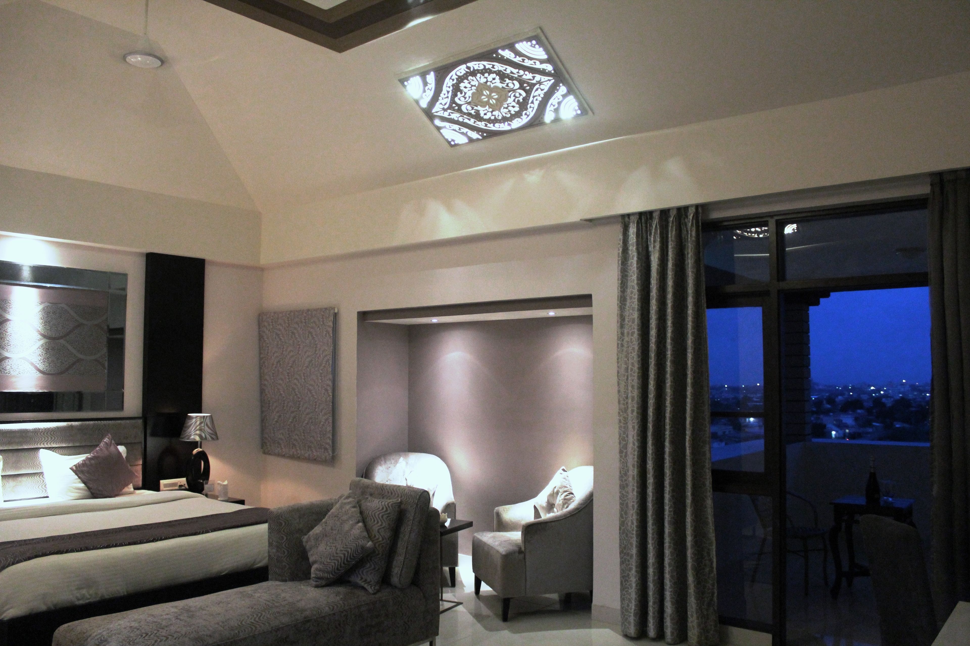 A modern hotel room with a large bed, a sofa, a chair, and a balcony with a city view.