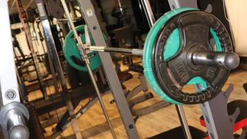 Un gimnasio con equipo de levantamiento de pesas, bancos y piso de madera.