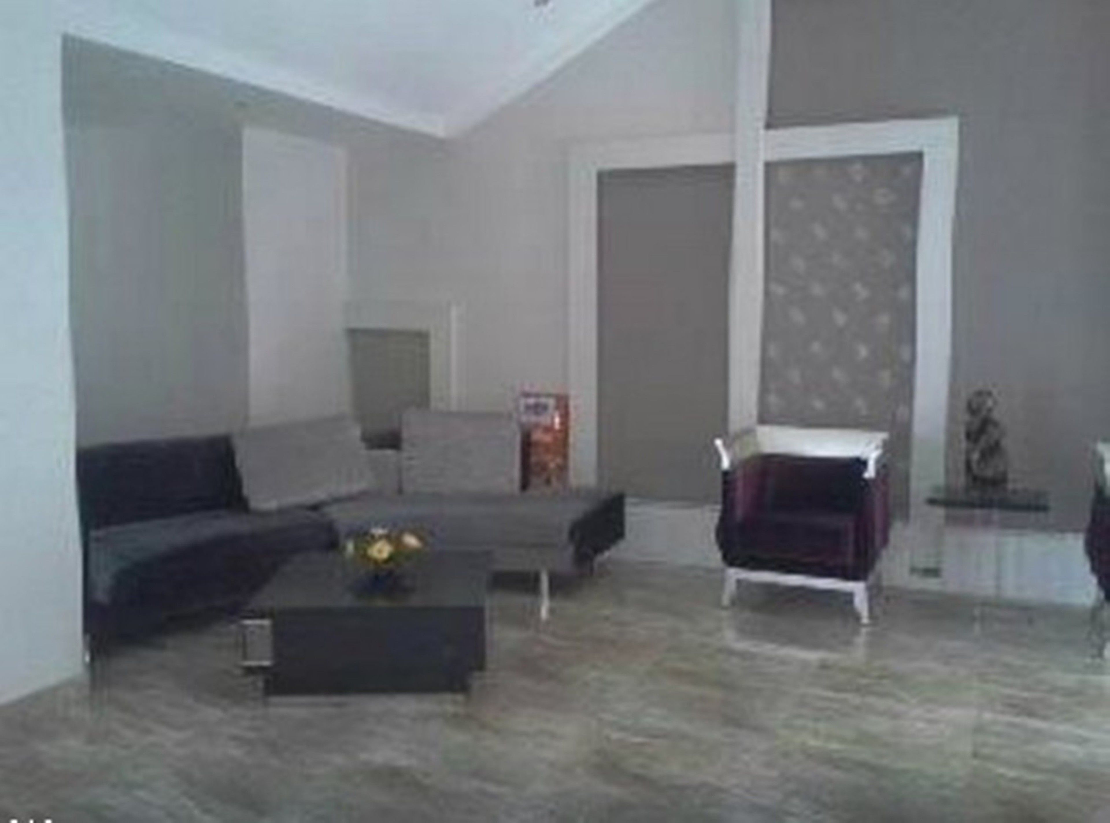 A modern living room with a grey sofa, a coffee table with a vase, and a dark armchair.