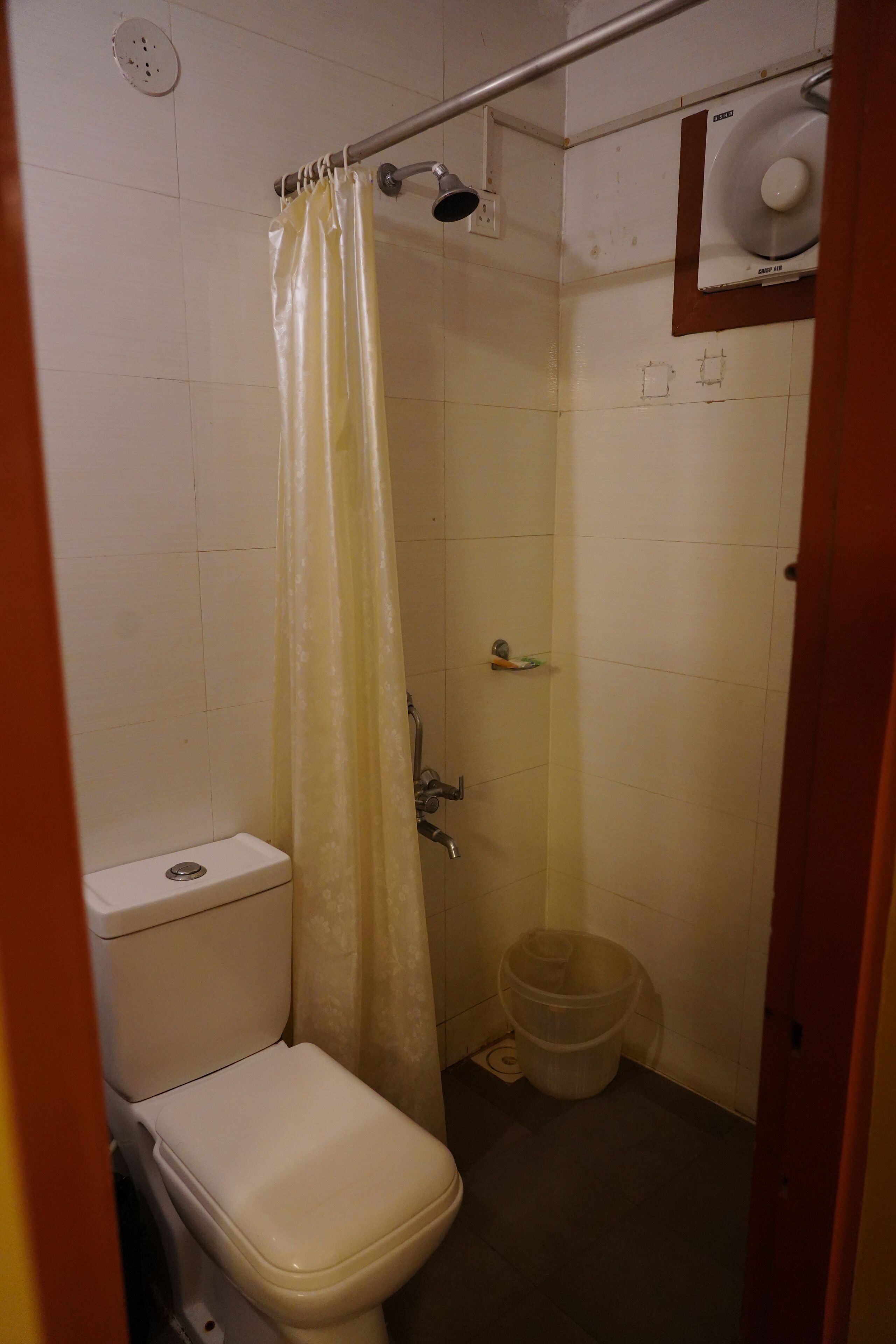 Ein kleines, schlichtes Badezimmer mit Toilette, Dusche und einem Plastikmülleimer.