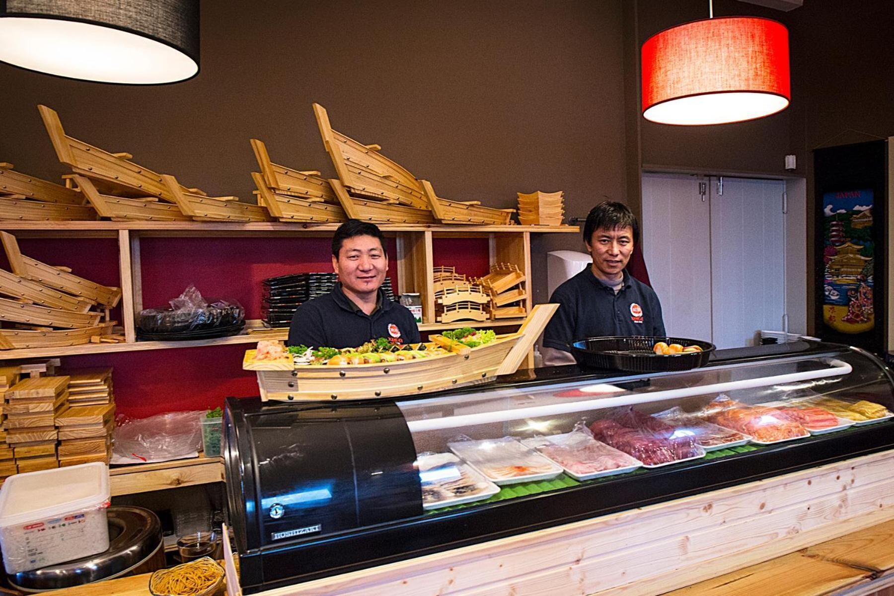 En sushibar med trästolar och ett kylskåp där färska skaldjur visas upp.