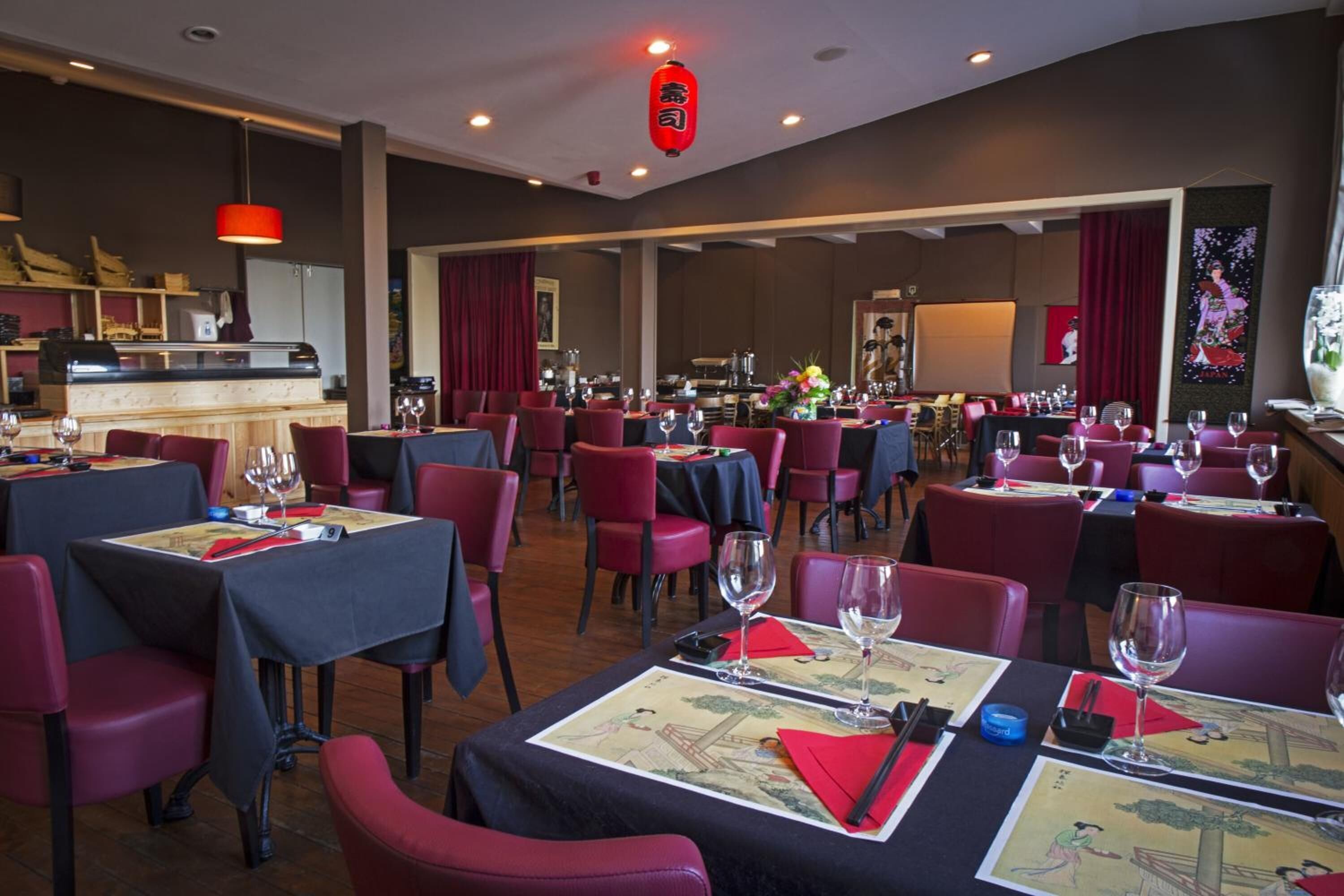 A restaurant with tables set for dining, red chairs, and a bar area in the background.