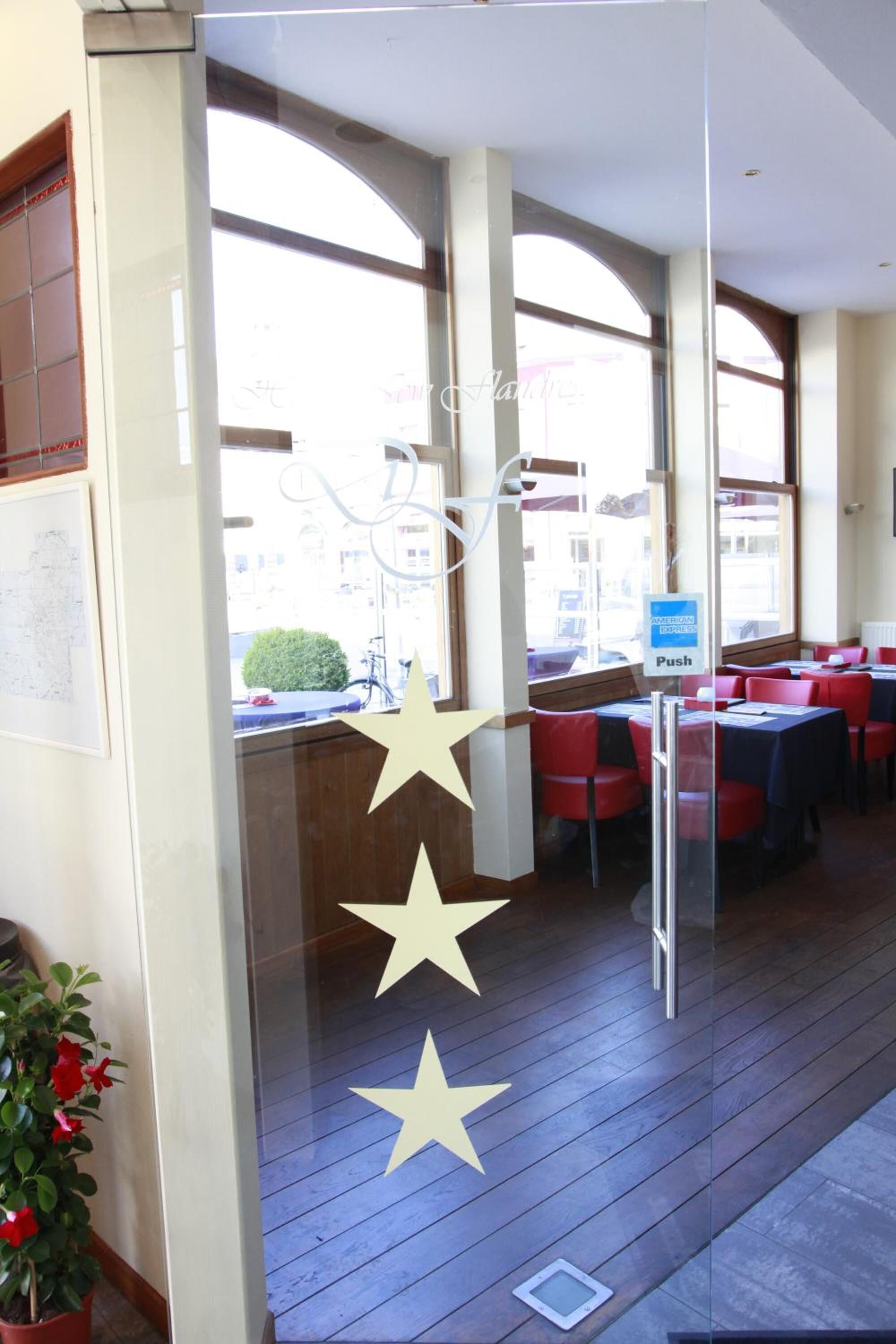 L’intérieur d’un restaurant avec des cloisons en verre, des chaises rouges et des tables.
