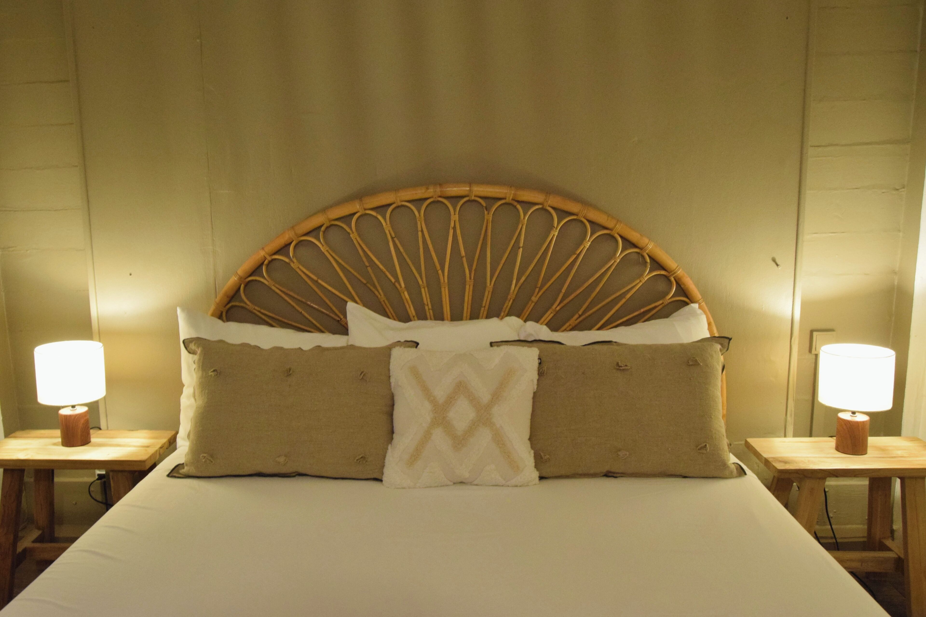 A bed with a woven headboard, two bedside tables with lamps, and three pillows.