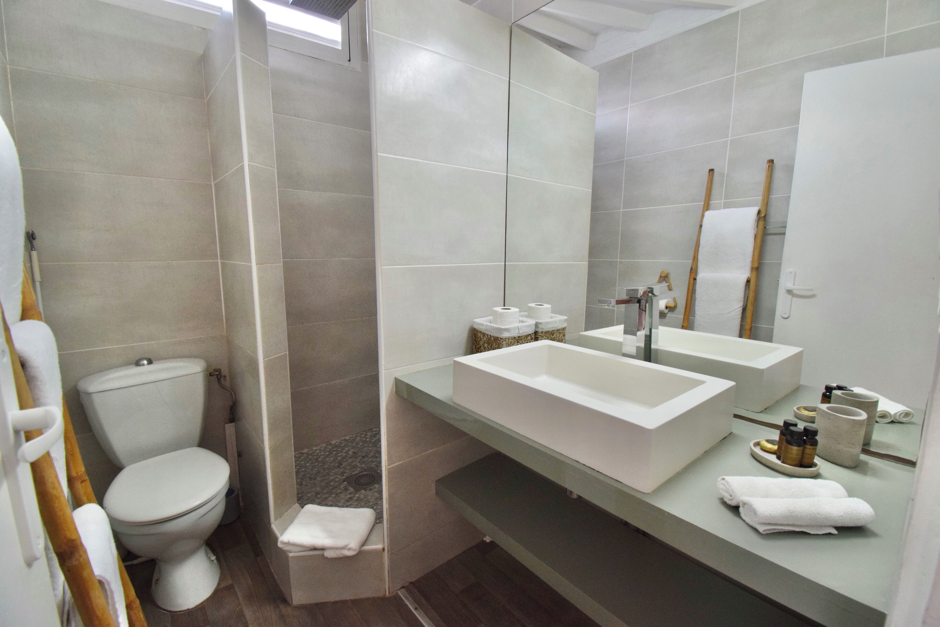 Un baño moderno con inodoro, ducha y tocador doble con un espejo grande.