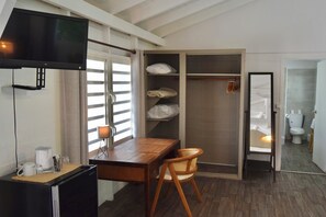 Una habitación con escritorio de madera, una silla, un televisor, un armario y un baño visible a través de una puerta abierta.