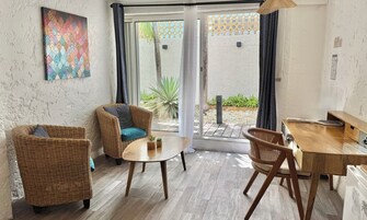 Habitación con mobiliario de mimbre, una pequeña mesa y vista a un área exterior con plantas y un muro con diseño.