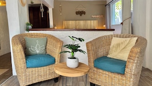 A reception area with two wicker chairs, a small round wooden table, and a potted plant. - KOHO-SXM (Grand Case)
