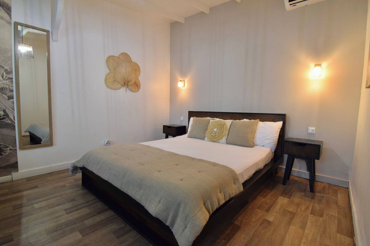 A bedroom with a large bed, two bedside tables, a wall-mounted fan, and two wall sconces.