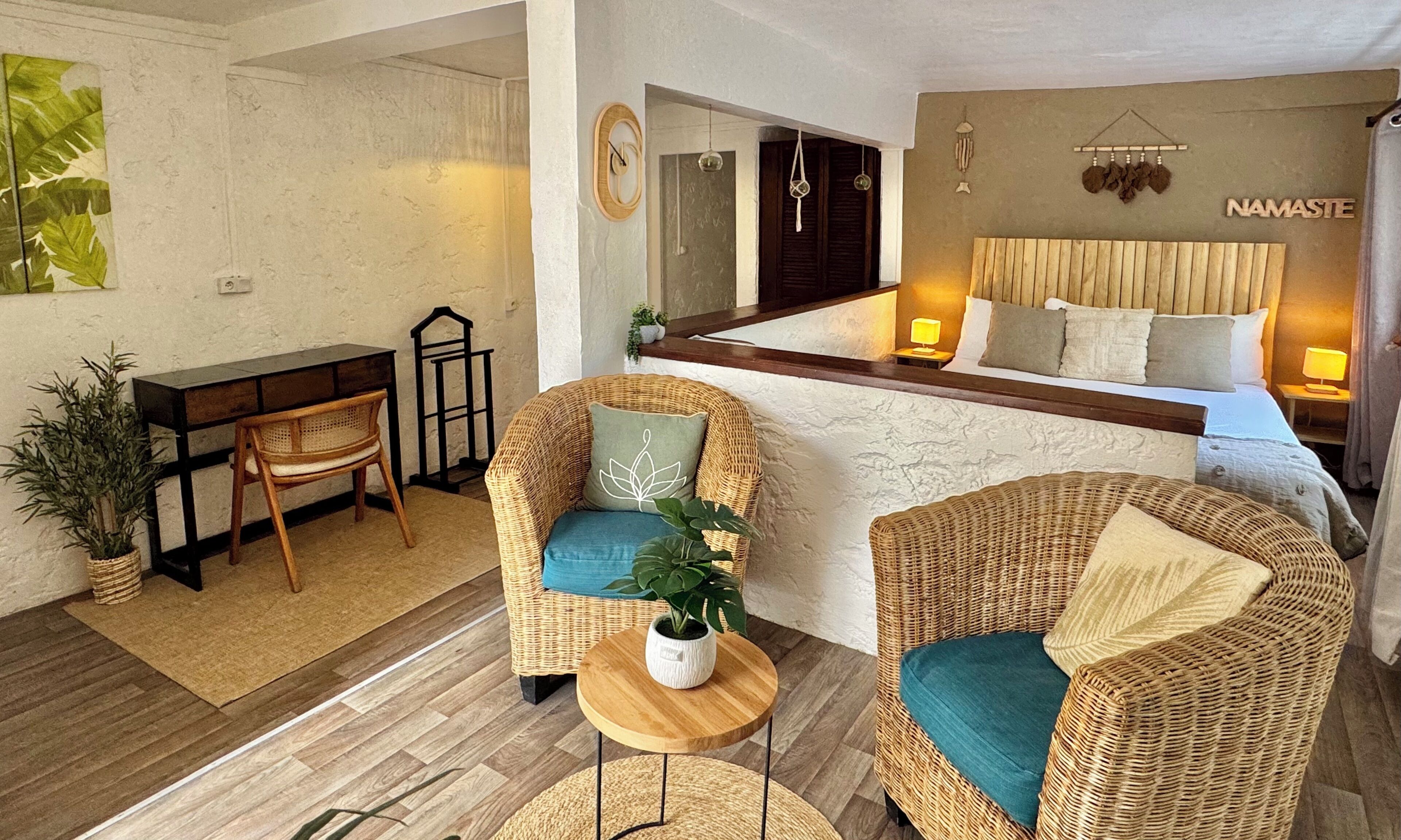 A modern hotel room with a bed, two wicker chairs, a small table, and a desk.