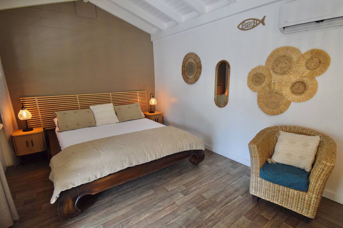A bedroom with a wooden bed, bedside lamps, a wicker chair, and decorative wall art.