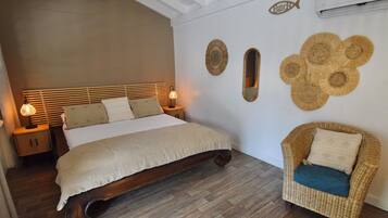 Un dormitorio con una cama de madera, lámparas de noche, un sillón de mimbre y decoración en la pared.