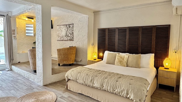 A spacious bedroom with a large bed, a wicker chair, and a view of the outdoors. - KOHO-SXM (Grand Case)