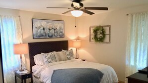 Une chambre à coucher avec un lit, deux lampes de chevet, un ventilateur de plafond, un tableau et une guirlande décorative accrochée au mur.