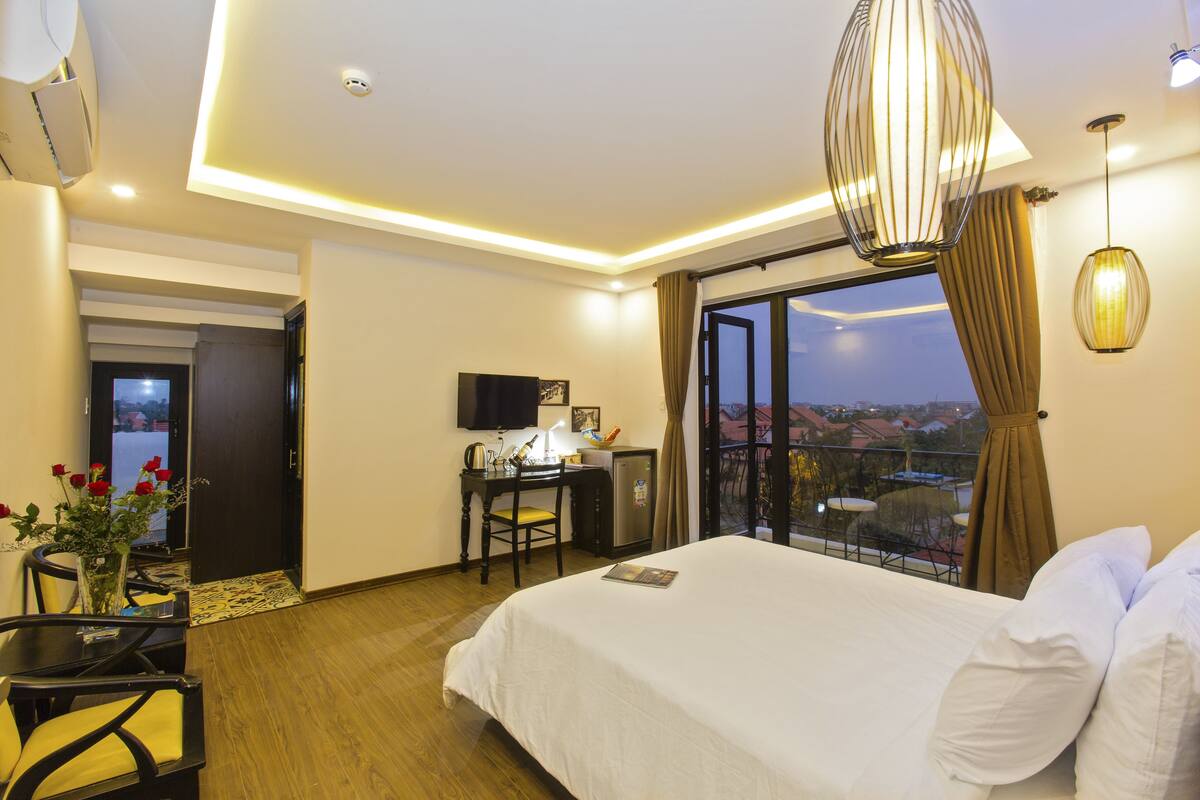 A hotel room with a bed, desk, and chair, a window with curtains, and a view of the outside.