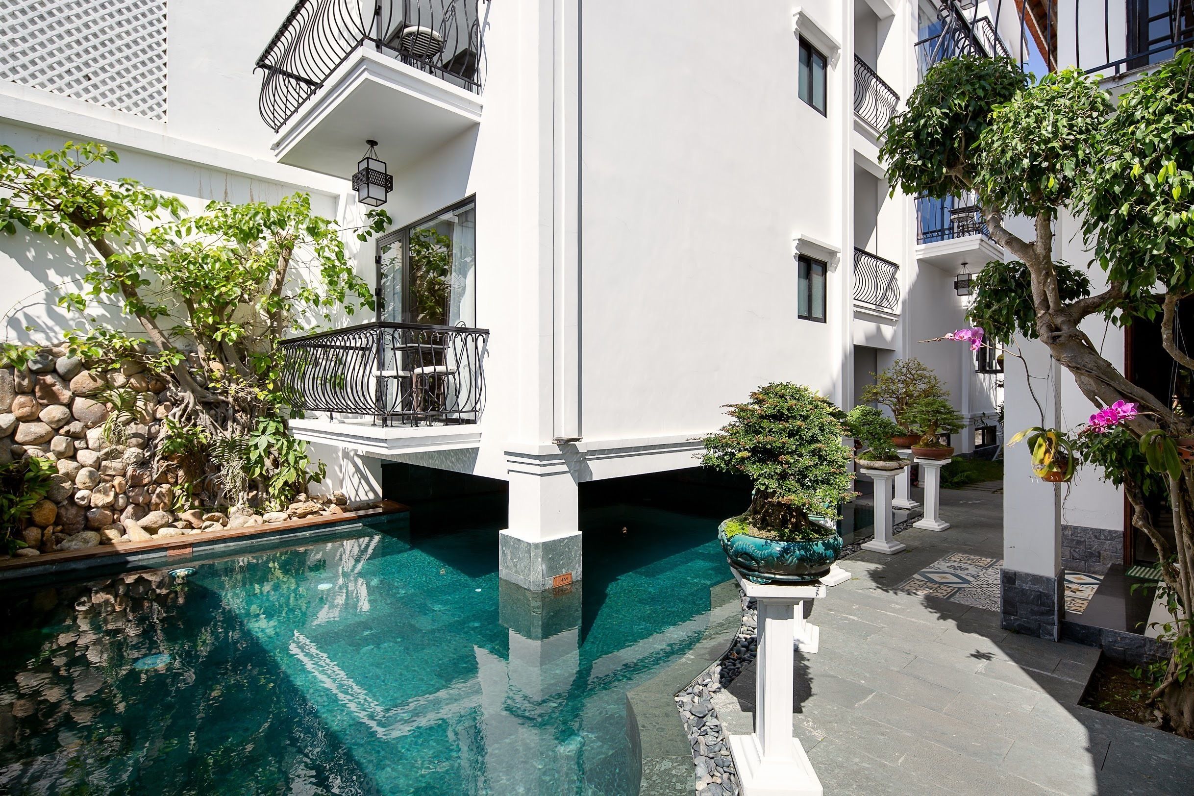 Un área de piscina con agua cristalina, rodeada de edificios blancos con balcones y plantas en macetas.