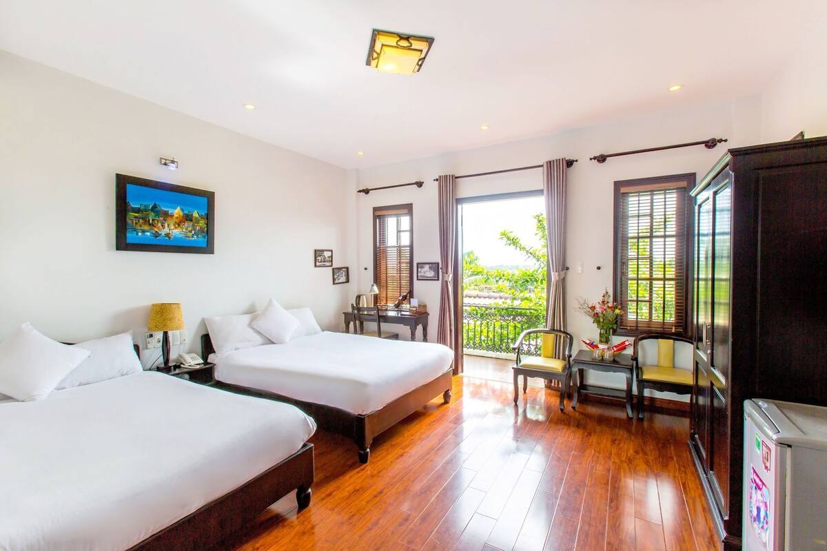 A hotel room with two beds, a desk, a chair, a balcony with a view, and a refrigerator.