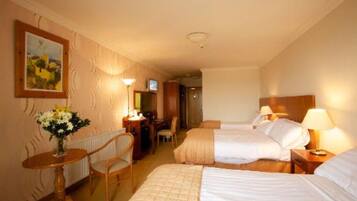 Habitación de hotel con dos camas, un escritorio con silla, una mesita con un jarrón de flores y un cuadro en la pared.