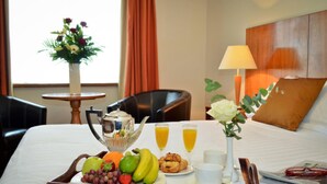 Uma bandeja de café da manhã bem arrumada com frutas, doces e bebidas sobre uma cama de hotel.