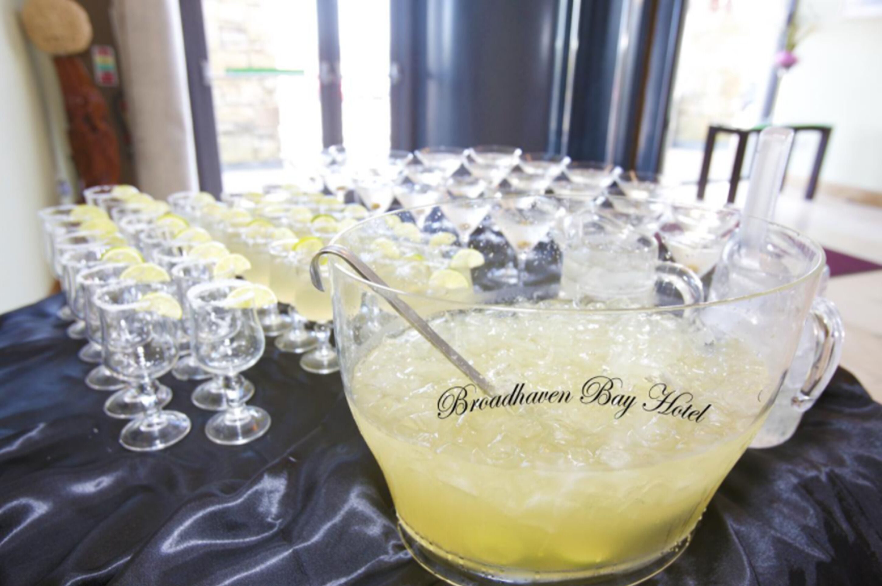 Une table sur laquelle sont disposés plusieurs verres contenant une boisson jaune, dont certains sont garnis de rondelles de citron, ainsi qu'une grande carafe portant l'inscription « Broadhaven Bay Hotel ».